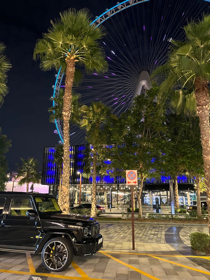 a car parked in front of a ferris wheel at night with palm trees and lights