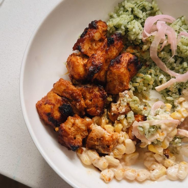 a white plate topped with chicken, rice and veggies next to coleslaw