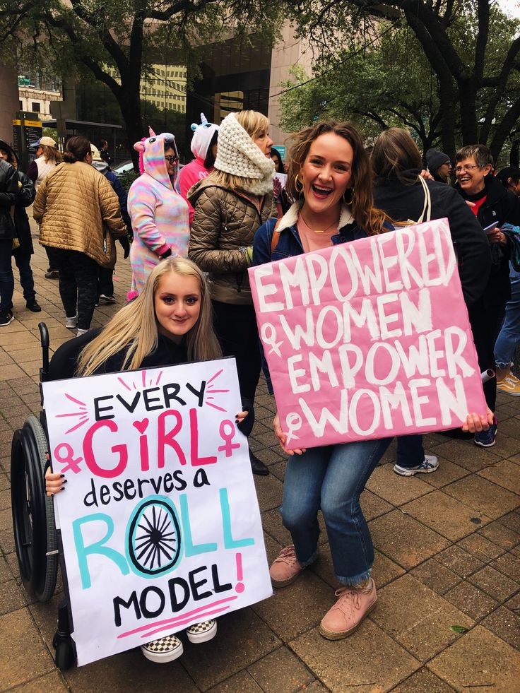 two women holding signs in front of a crowd