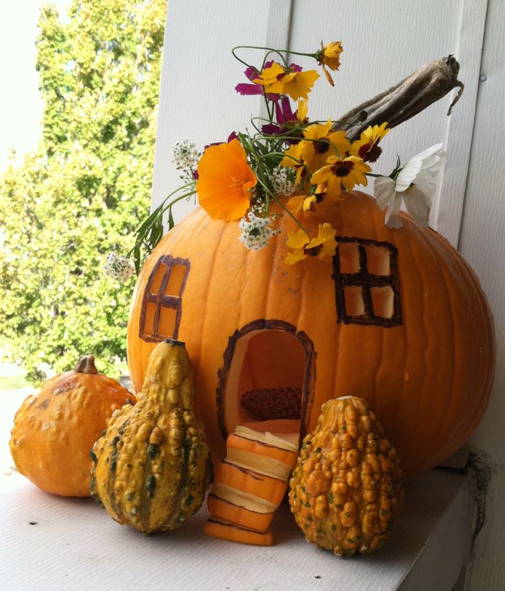 a pumpkin shaped house sitting on top of a window sill with flowers in it