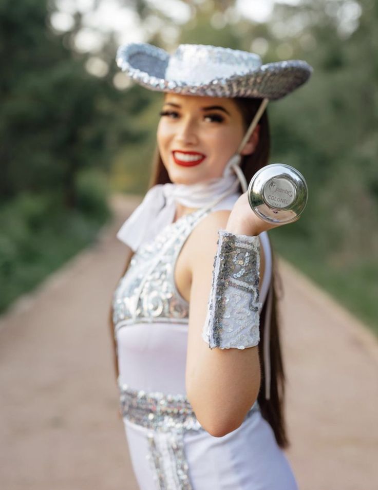 a woman in a white dress and silver hat holding a can with her right hand