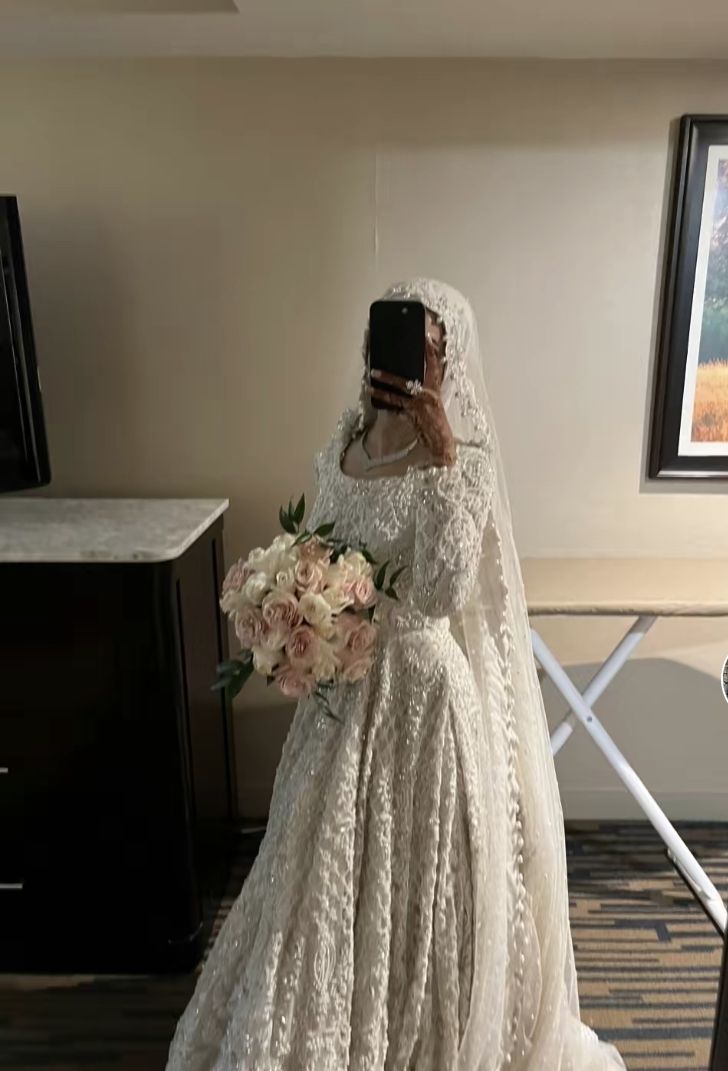 a woman in a wedding dress taking a photo with her cell phone while wearing a veil