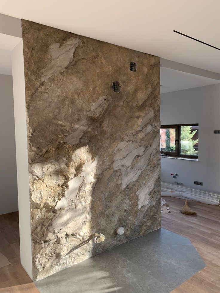 a large stone wall in the middle of a room with wood flooring and white walls