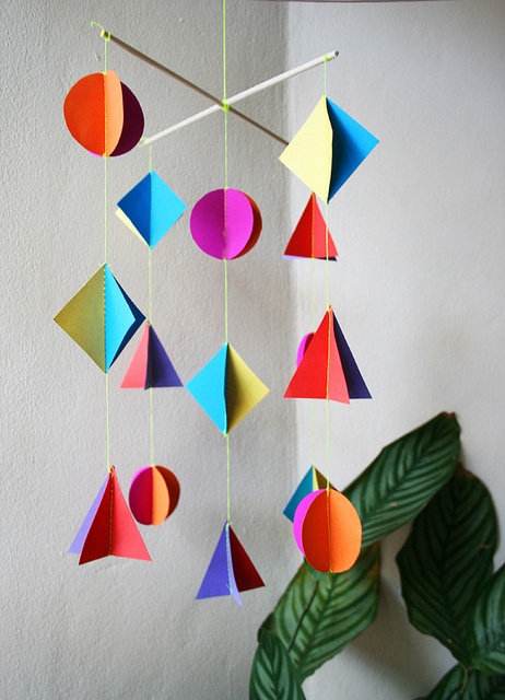 an origami mobile hanging on a wall next to a potted plant