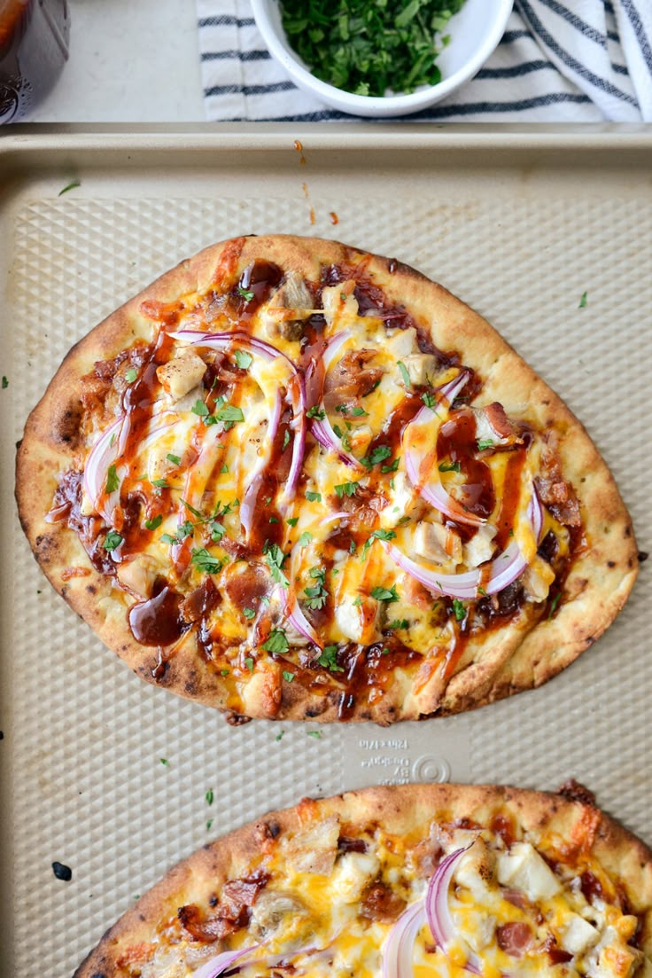 two pizzas sitting on top of a pan covered in cheese and onions next to a bowl of greens