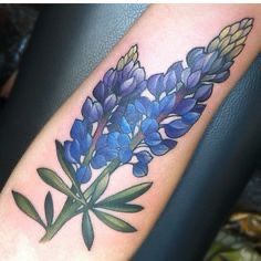 a blue flower with green leaves on the arm is shown in this tattoo style photo