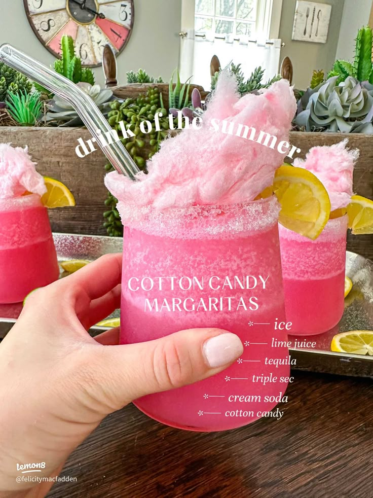 a person holding up a pink cocktail in front of two glasses with lemons on the rim