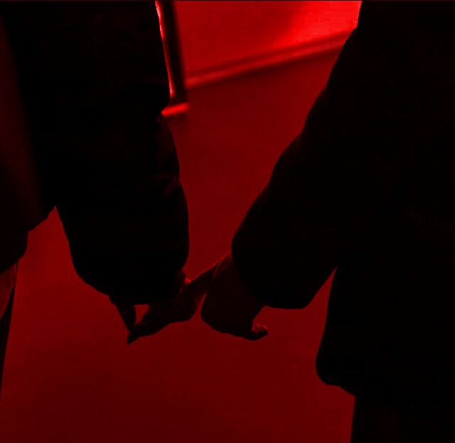 two people holding hands in front of a red light