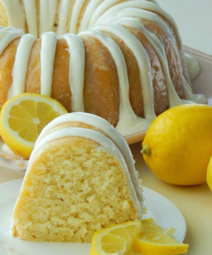 a lemon bunt cake with white icing on a plate next to sliced lemons