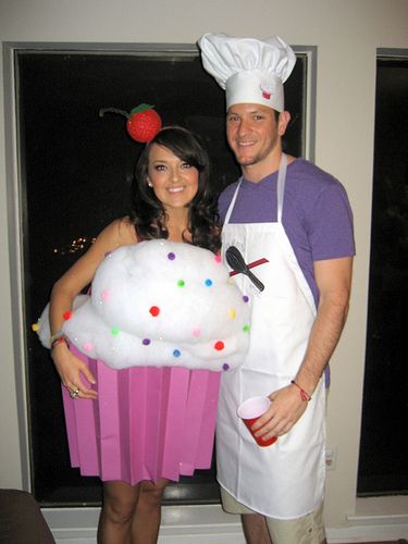 a man and woman dressed up in costumes standing next to each other holding a giant cupcake