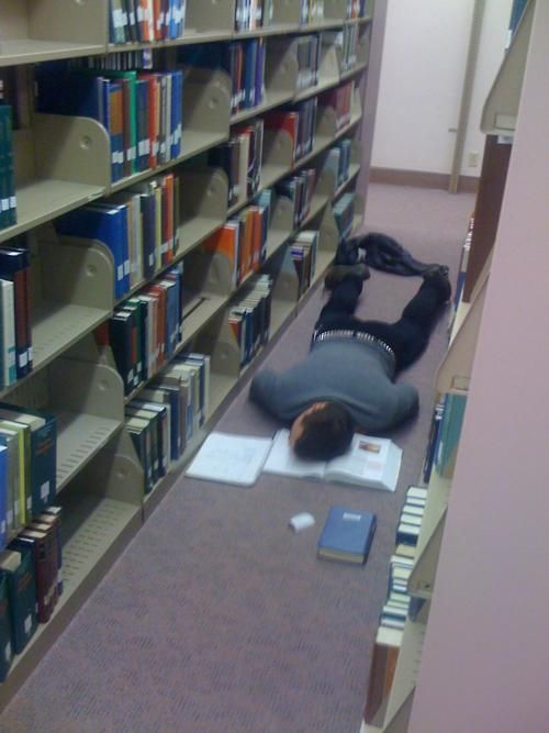 a person laying on the floor in front of a book shelf filled with books and papers