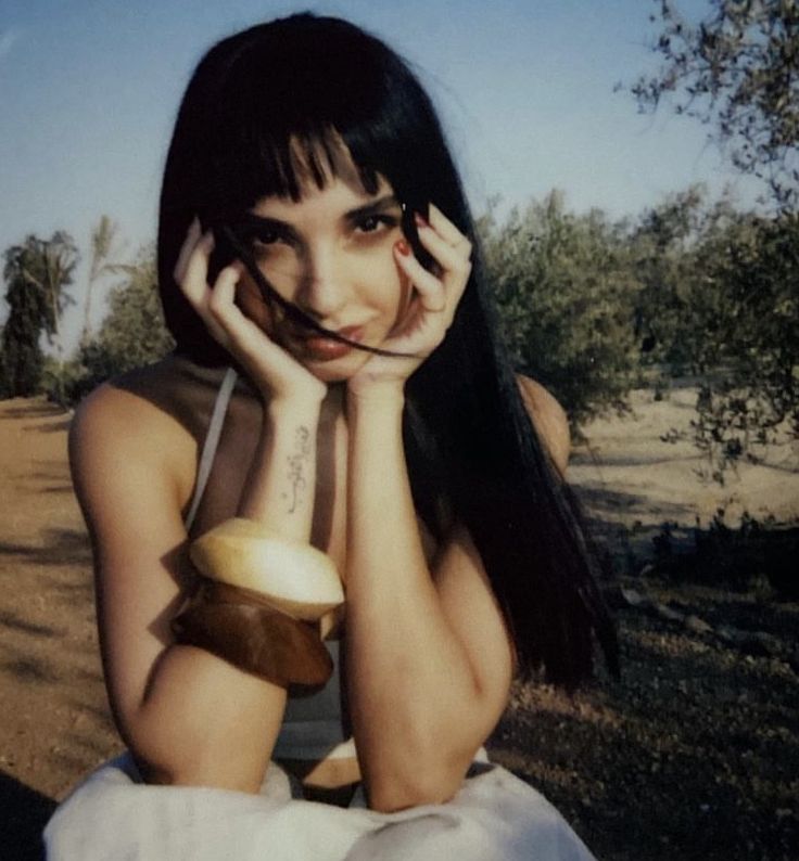 a woman sitting on the ground with her hands to her face and holding an apple in front of her face