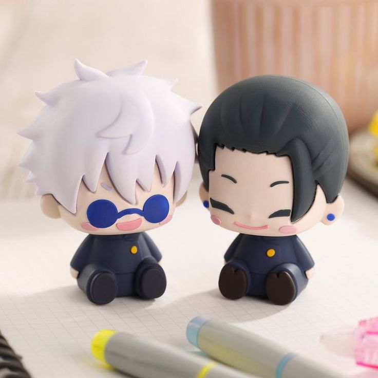 two anime figurines sitting next to each other on top of a white table