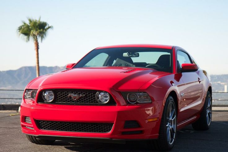 a red mustang is parked on the side of the road near some water and palm trees