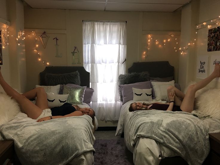 two people laying on their beds in a room with lights strung above the bed and windows