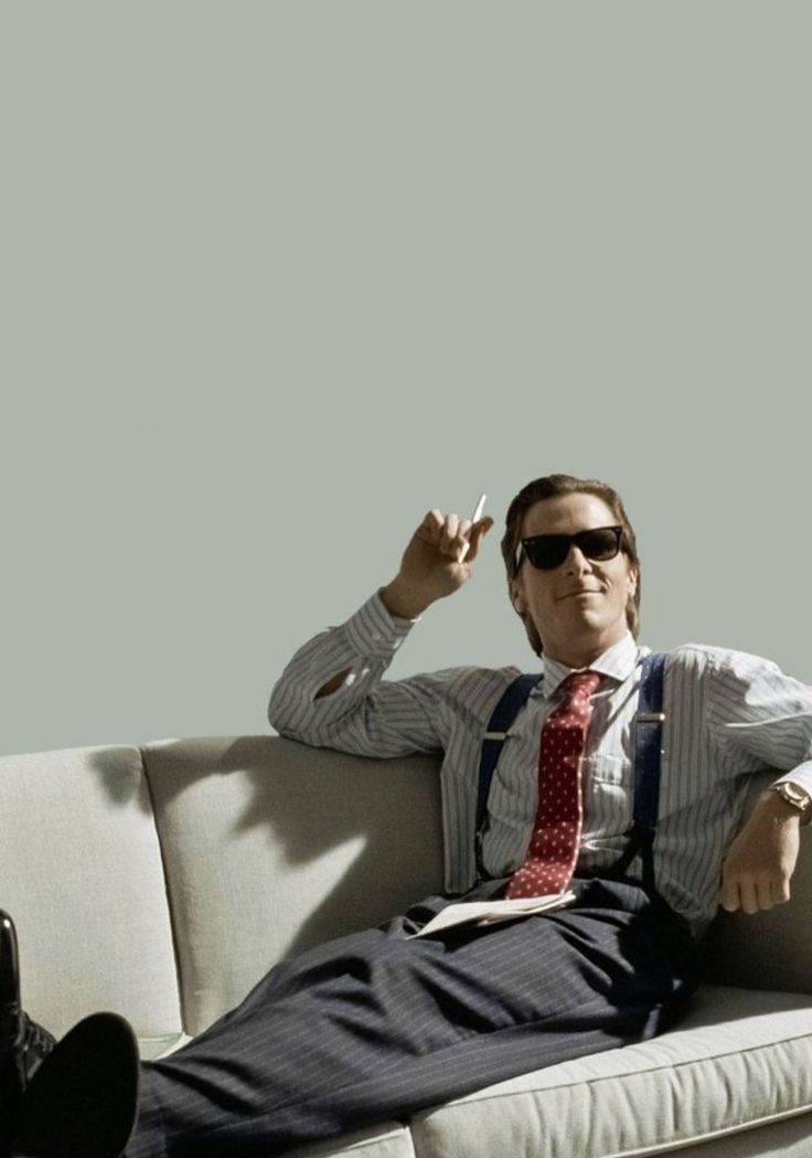 a man sitting on top of a white couch wearing sunglasses and a red neck tie