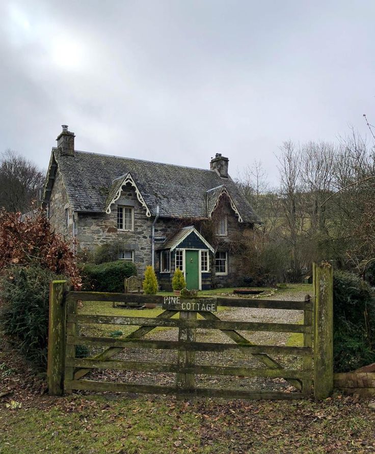 an old stone house with a green door and gate in the foreground, on a cloudy day