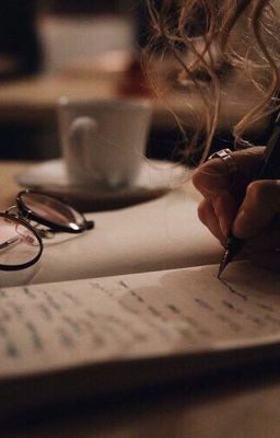 a person writing on a piece of paper next to a coffee cup and eyeglasses