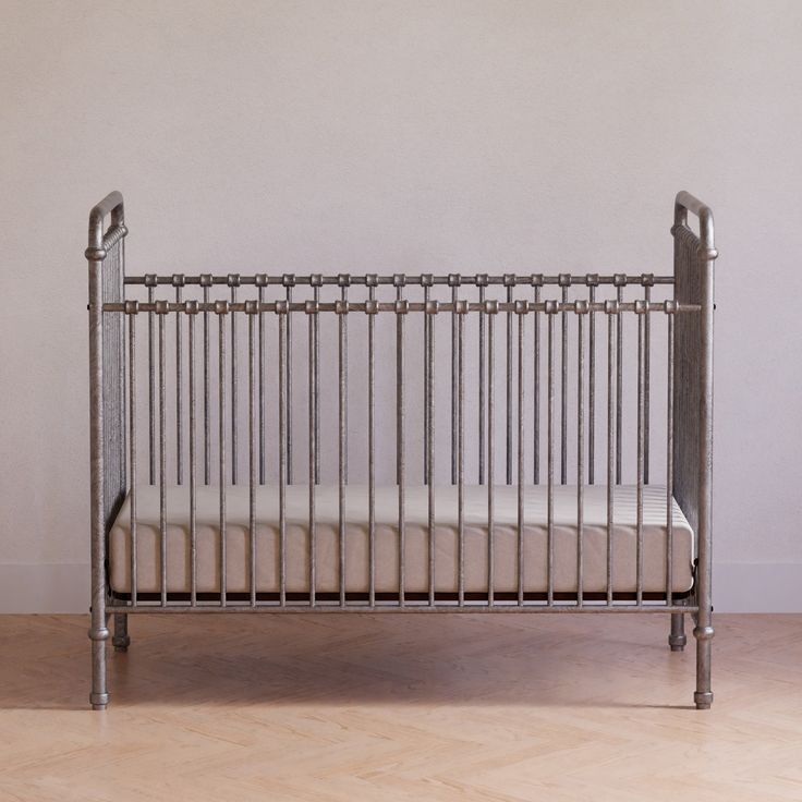 a metal crib sitting on top of a hard wood floor next to a wall