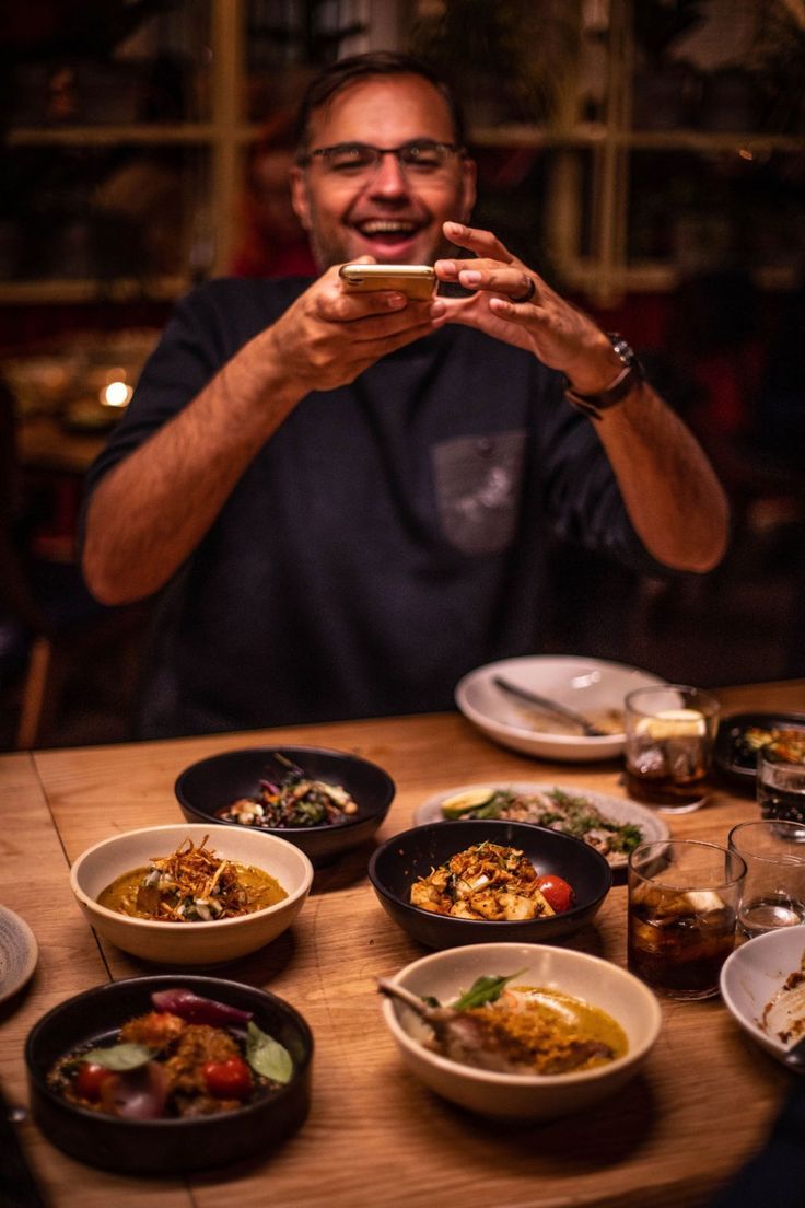 a man sitting at a table with many plates of food in front of him and taking a selfie