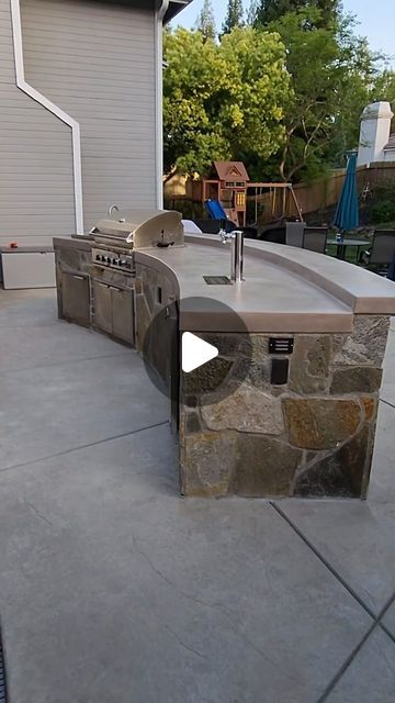 an outdoor kitchen with grill and sink in the middle of a patio area next to a house