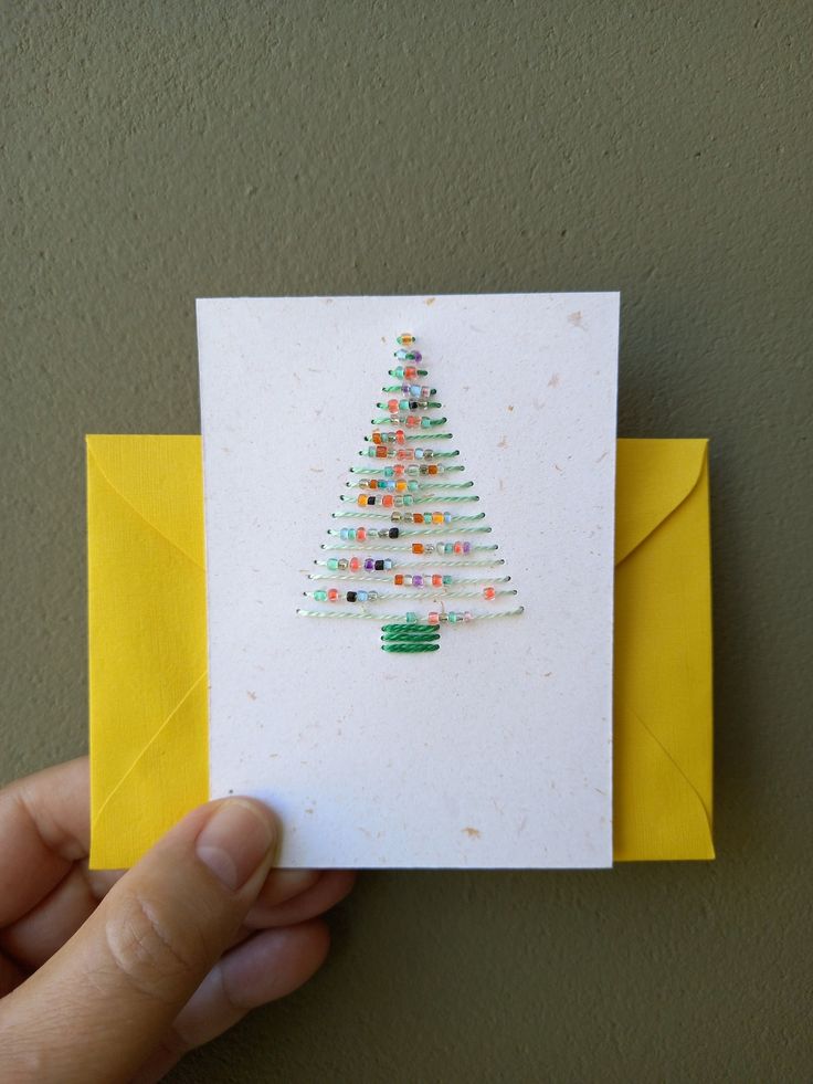 a hand holding up a card with a christmas tree on the front and yellow envelope