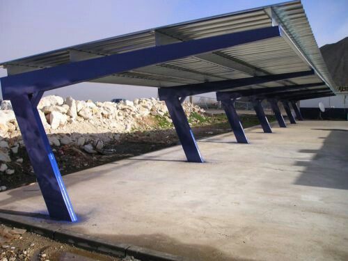 an empty covered parking lot with rocks and gravel in the foreground, under a blue metal roof