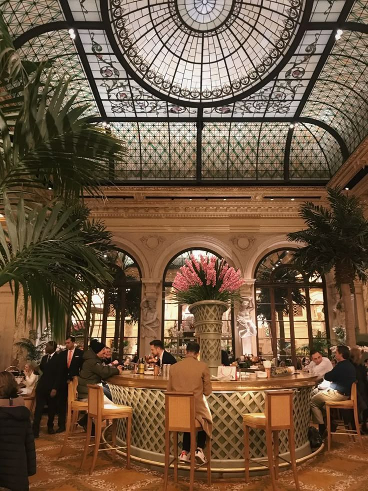 people are sitting at tables in the middle of an ornately decorated room with glass ceiling