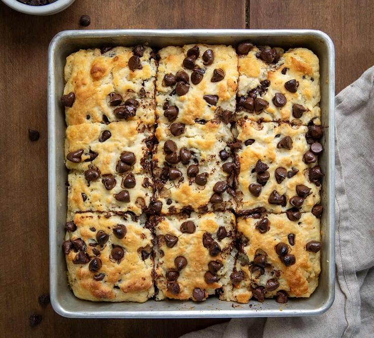 a pan filled with bread and chocolate chips on top of a wooden table next to a cup of coffee