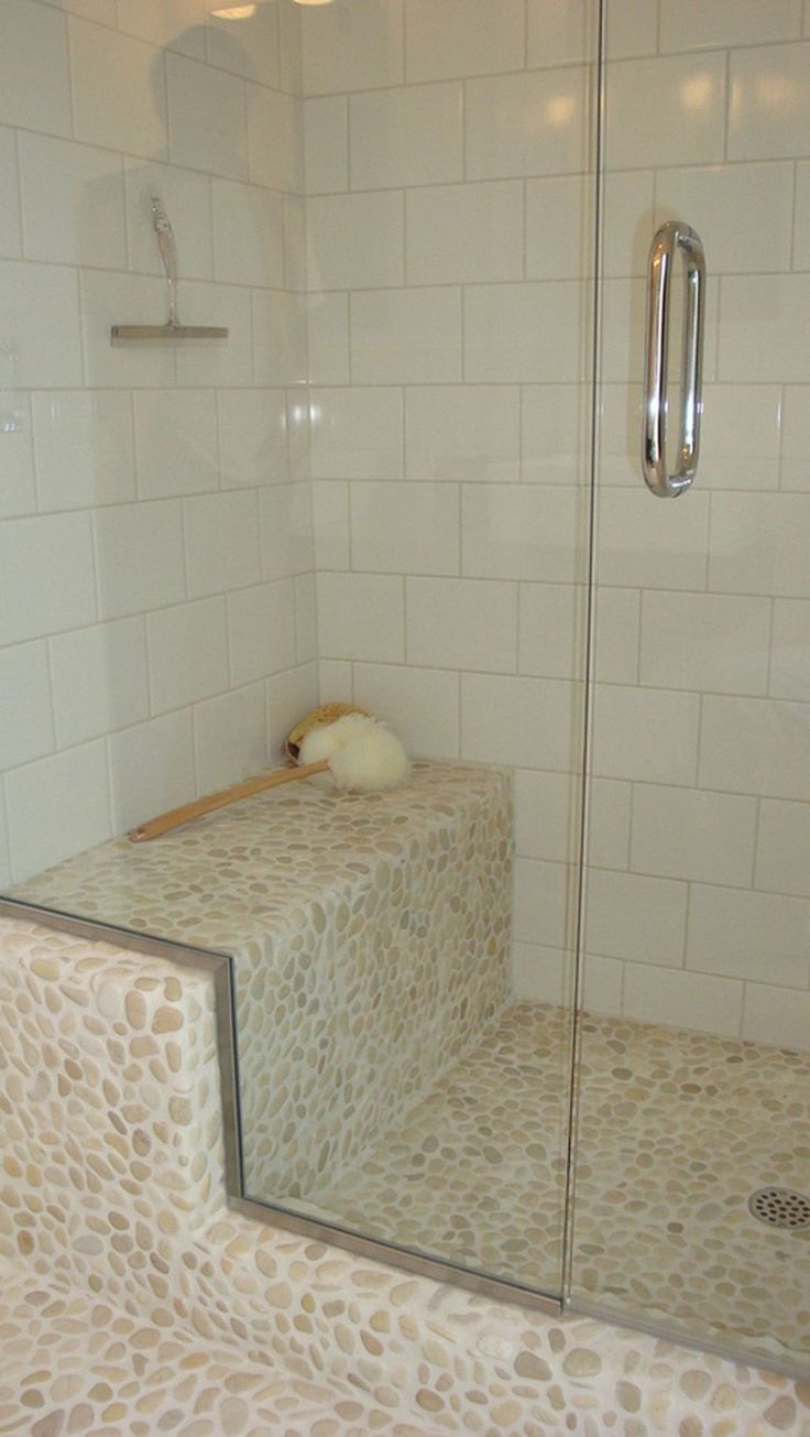 a walk in shower sitting next to a white tiled wall and counter top with a glass door