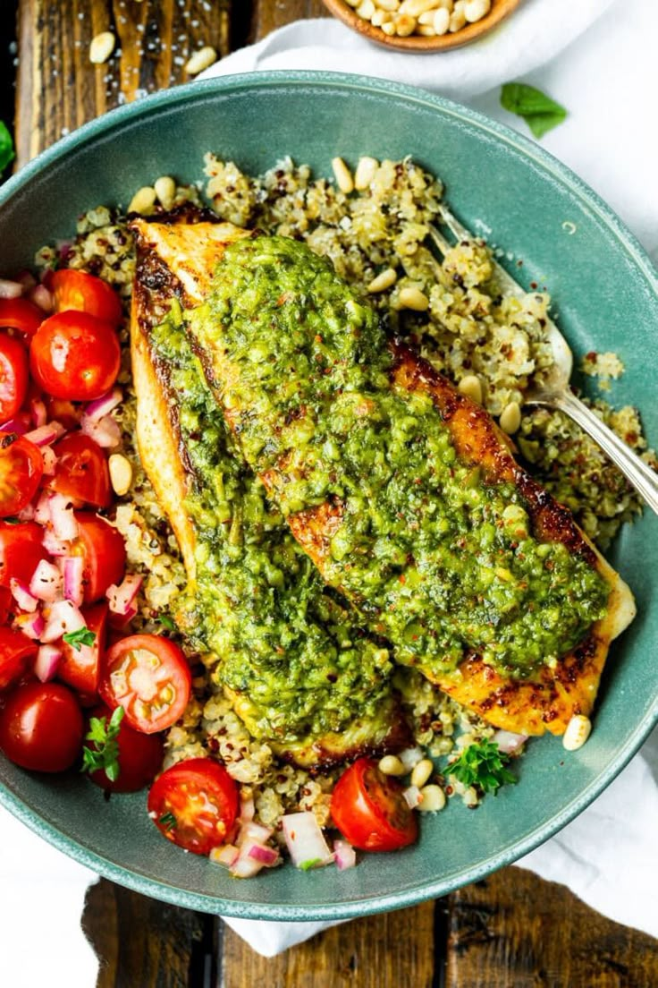 a blue bowl filled with chicken, rice and tomatoes on top of a wooden table