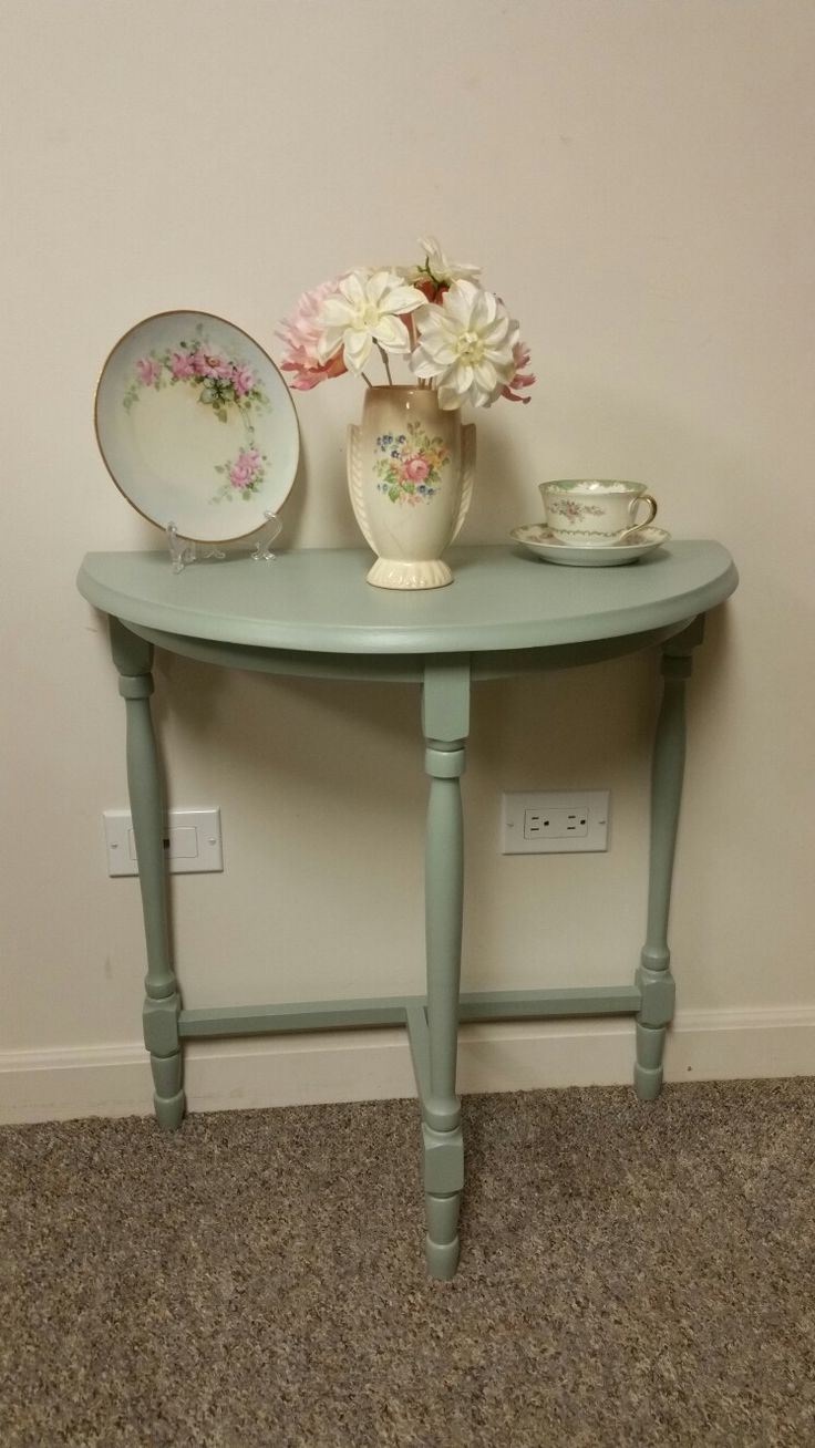 there is a vase with flowers on it next to a plate and cup sitting on a table