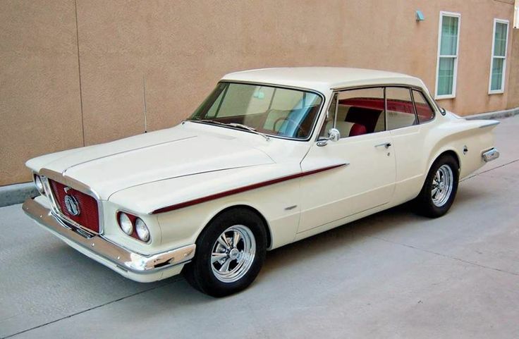 an old white car is parked in front of a tan building with red trim on it