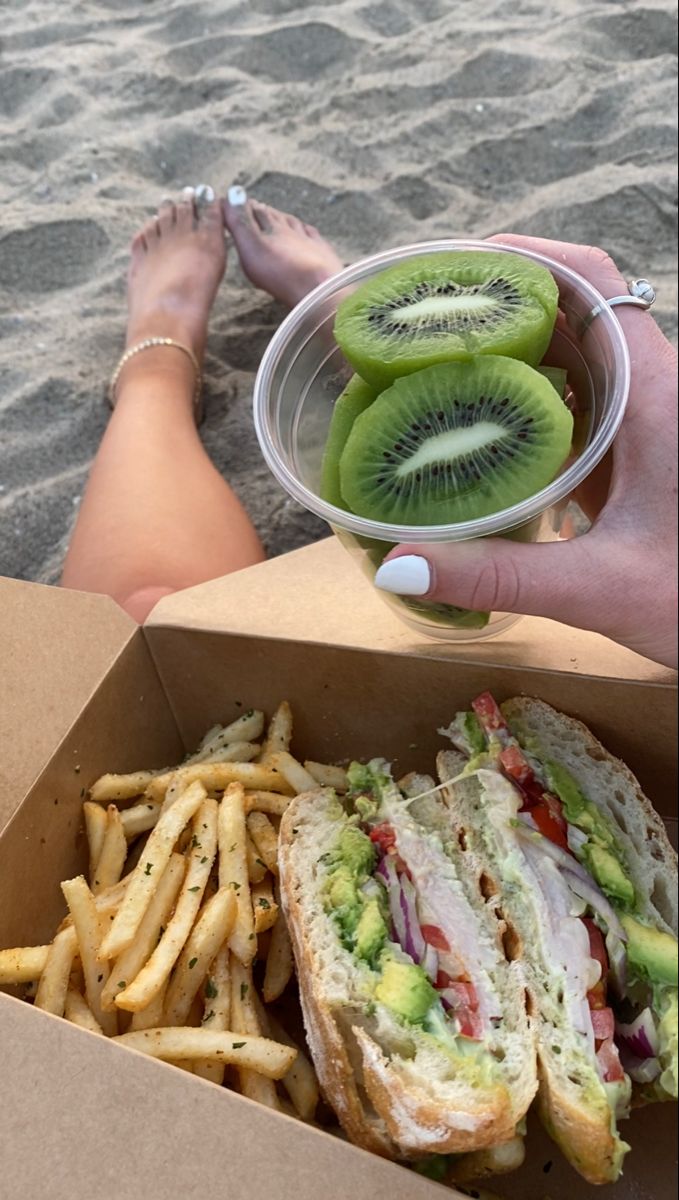 a person sitting on the beach with a sandwich and french fries