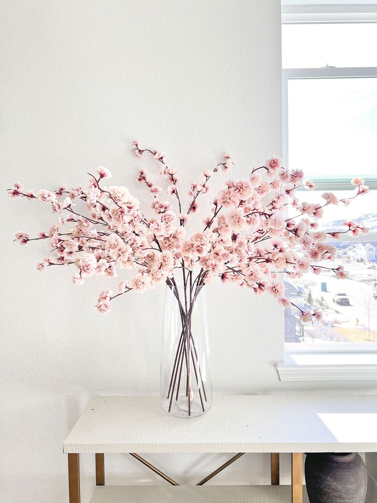 a vase filled with pink flowers sitting on top of a white table next to a window