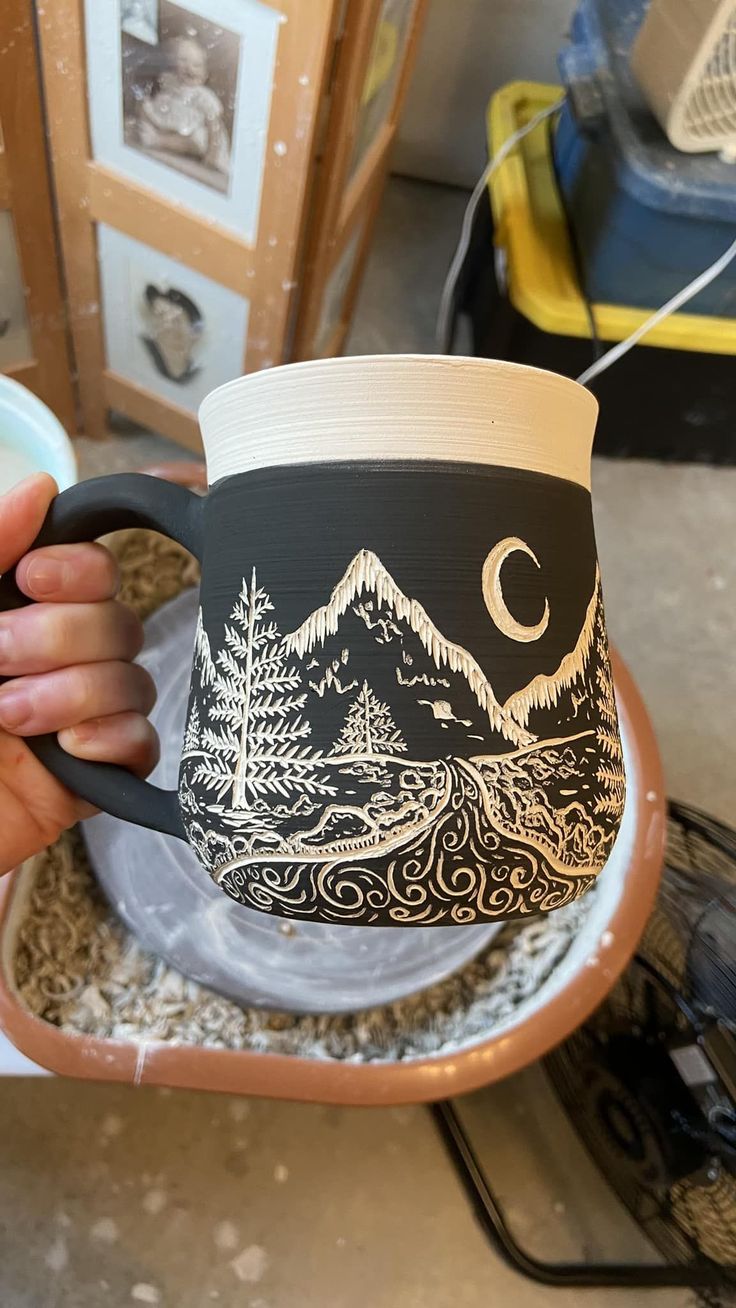 a person holding a coffee mug with mountains and trees on it