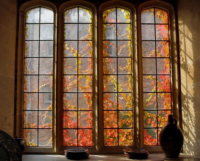 the sun shines through three windows in an old building with autumn foliage on them