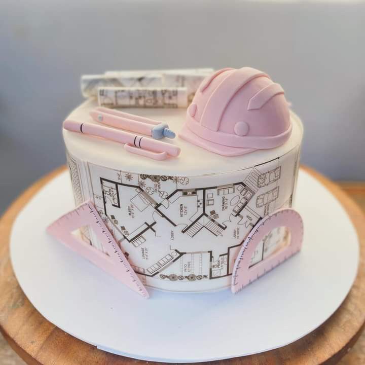 a cake made to look like a house with construction plans on top and pink trimmings