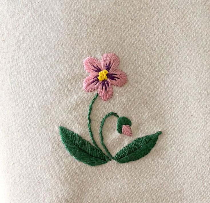 a pink flower with green leaves is embroidered onto a white piece of cloth that has been stitched together