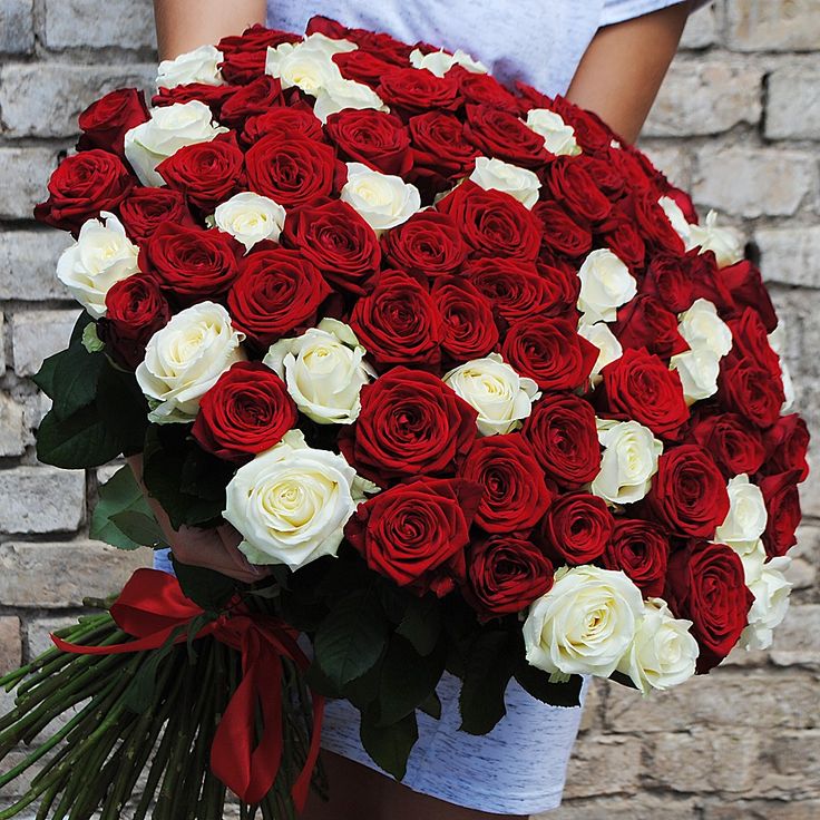 a woman holding a large bouquet of red and white roses in front of a brick wall