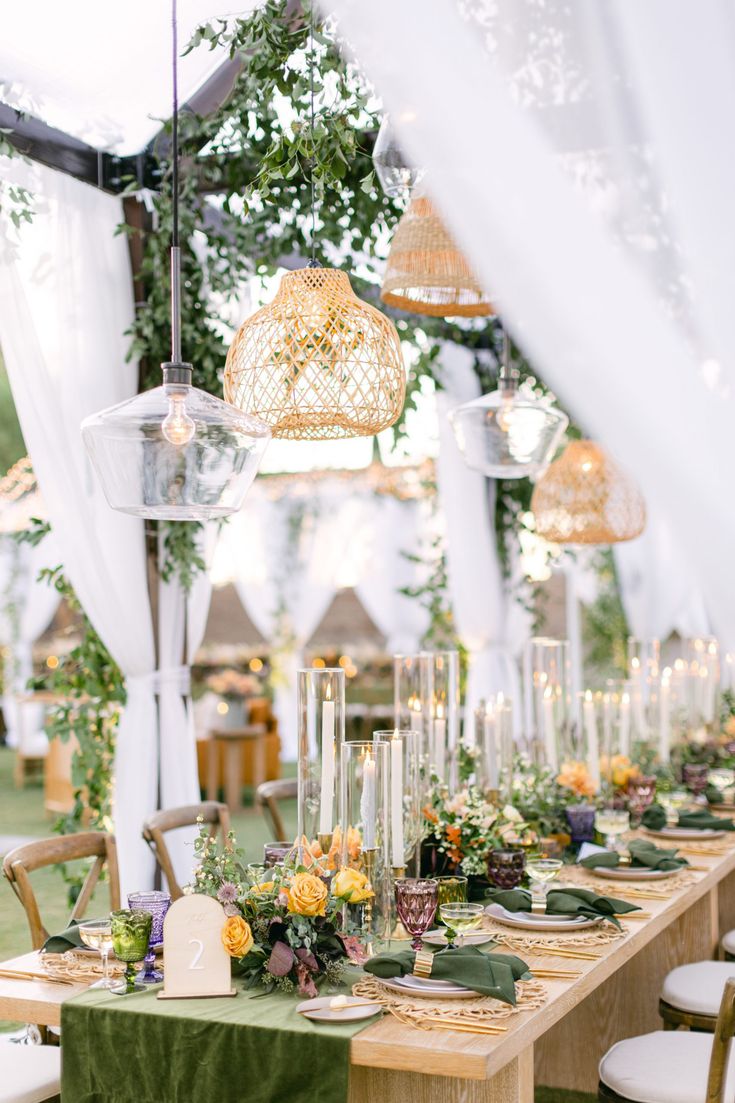 a table set up with candles, flowers and greenery for an outdoor wedding reception