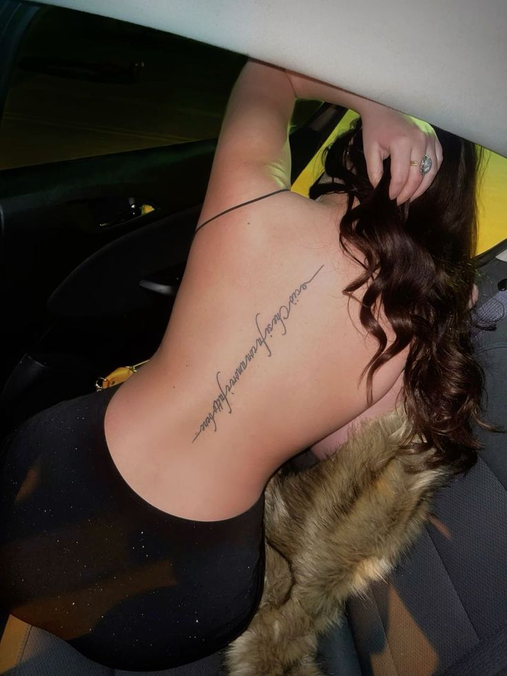 a woman sitting in the back seat of a car with her tattoo on her lower back