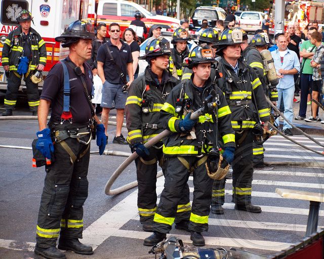 several firemen are standing in the street with hoses on their laps and people watching