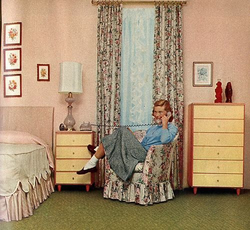 a woman sitting in a chair talking on a cell phone next to a dresser and bed