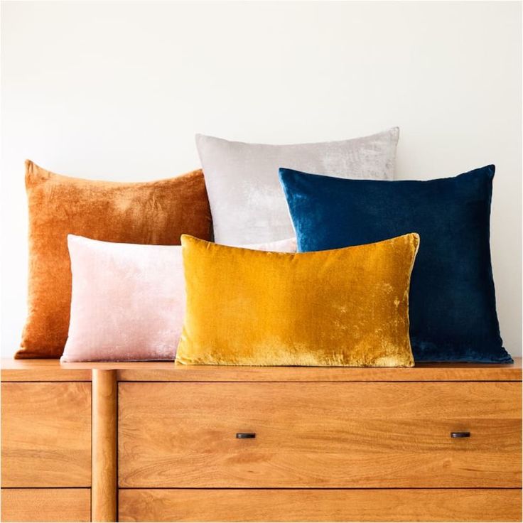 four different colored pillows sitting on top of a dresser