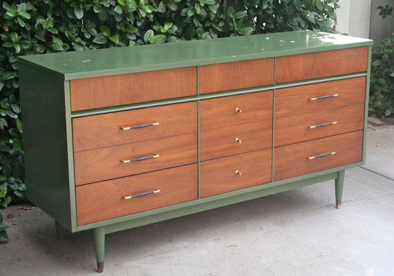 a green and brown dresser sitting in front of a bush