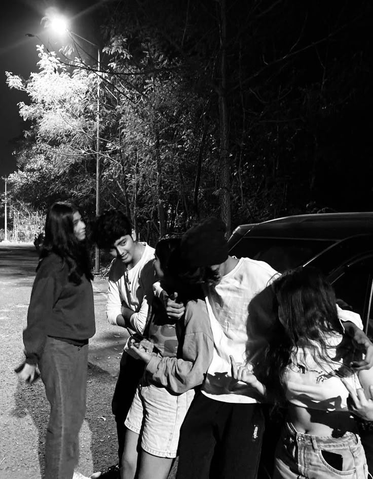 several people are standing around talking to each other in front of a car at night