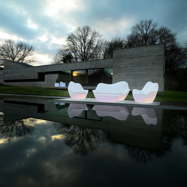 two white chairs sitting next to each other on the side of a body of water