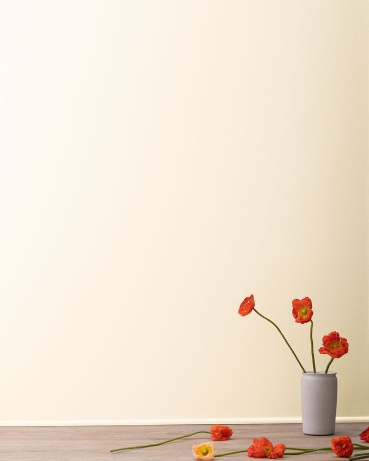 some red flowers in a white vase on a wooden floor next to an empty wall