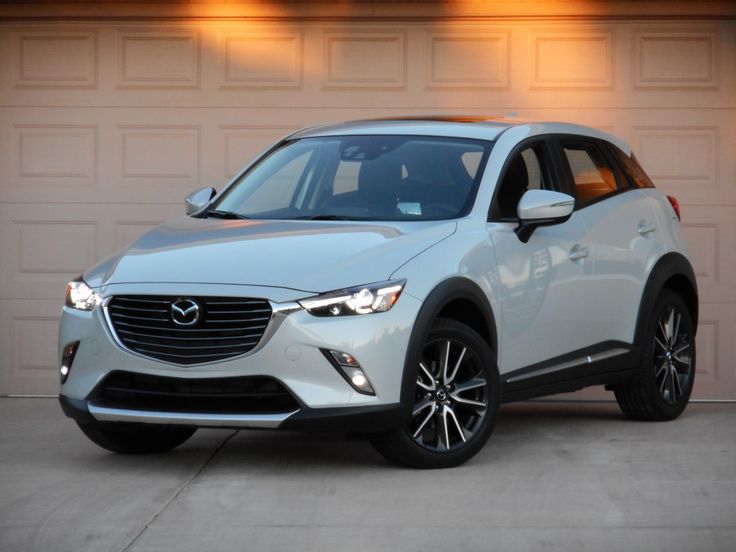 a white mazda cx - 3 parked in front of a garage with its lights on